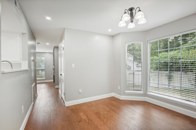 unfurnished room with a chandelier, wood-type flooring, and a healthy amount of sunlight