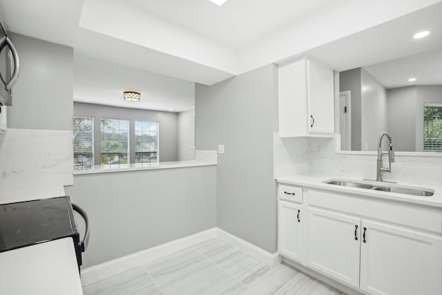 kitchen with kitchen peninsula, decorative backsplash, white cabinetry, range, and sink