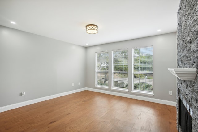 unfurnished living room featuring hardwood / wood-style flooring and a stone fireplace