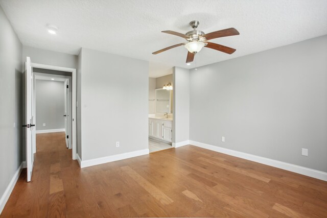 unfurnished bedroom with ensuite bathroom, a textured ceiling, light wood-type flooring, and ceiling fan with notable chandelier