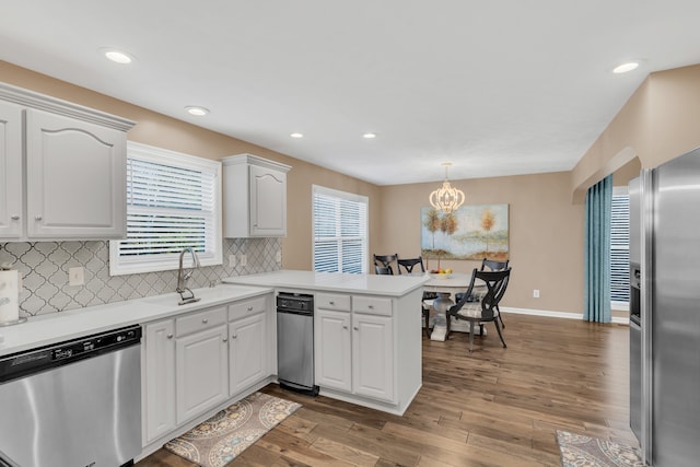 kitchen featuring dark hardwood / wood-style floors, kitchen peninsula, stainless steel appliances, decorative light fixtures, and white cabinetry