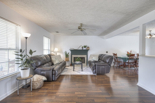 living room with a tile fireplace, a textured ceiling, ceiling fan with notable chandelier, and dark wood-type flooring