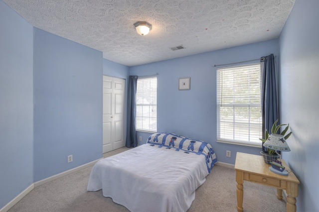 bedroom featuring multiple windows, a textured ceiling, light colored carpet, and a closet