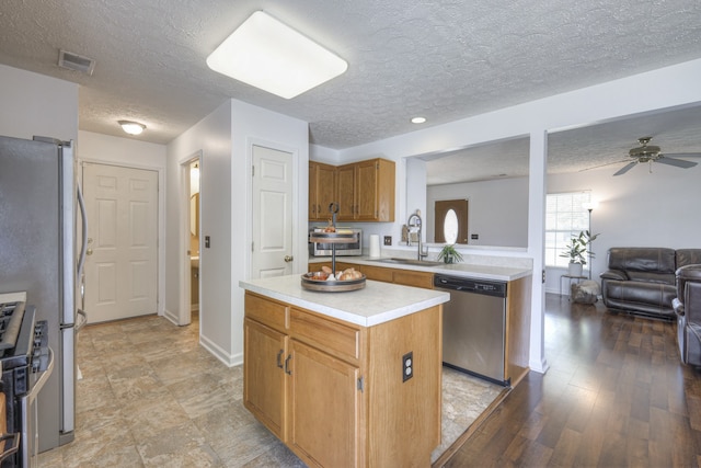 kitchen with ceiling fan, sink, a textured ceiling, a kitchen island, and appliances with stainless steel finishes