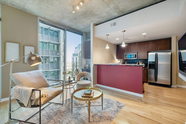 kitchen with decorative backsplash, appliances with stainless steel finishes, light wood-type flooring, pendant lighting, and dark brown cabinetry