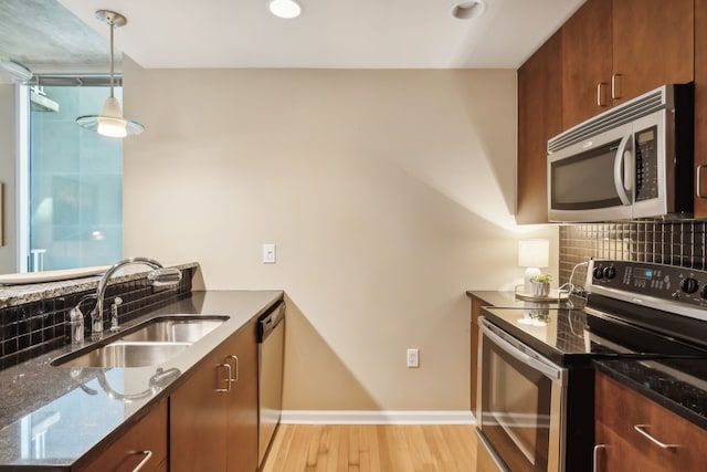 kitchen featuring backsplash, appliances with stainless steel finishes, dark stone countertops, light hardwood / wood-style floors, and sink