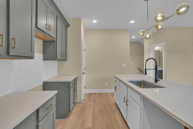 kitchen with gray cabinetry, hanging light fixtures, light stone countertops, sink, and light hardwood / wood-style flooring