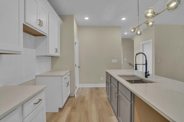 kitchen with sink, decorative light fixtures, white cabinetry, and light hardwood / wood-style flooring