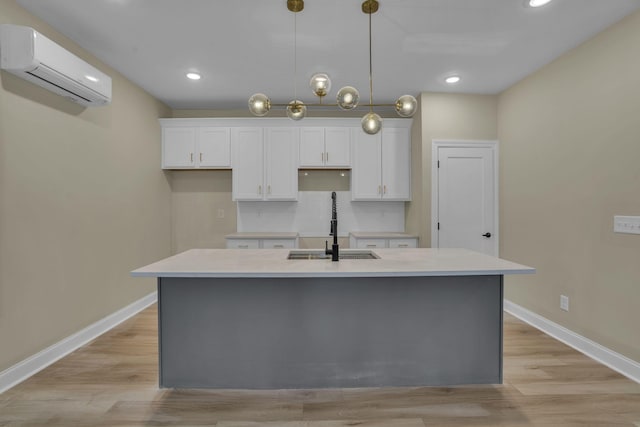 kitchen with white cabinetry, a kitchen island with sink, and an AC wall unit