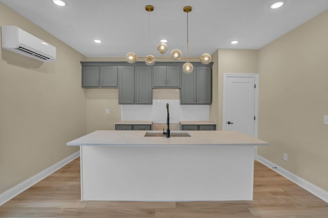 kitchen with sink, an island with sink, a wall mounted AC, pendant lighting, and gray cabinetry