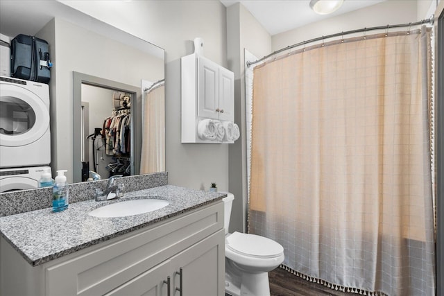 bathroom with stacked washer / drying machine, toilet, hardwood / wood-style floors, curtained shower, and vanity