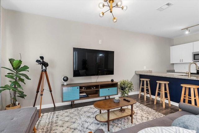 living room with dark wood-type flooring, an inviting chandelier, and sink