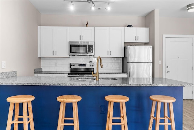 kitchen featuring appliances with stainless steel finishes, a breakfast bar, white cabinetry, light hardwood / wood-style floors, and sink