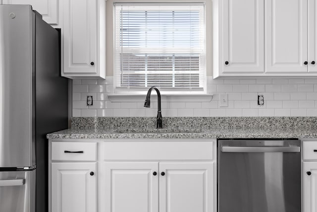 kitchen with white cabinets, light stone counters, backsplash, appliances with stainless steel finishes, and sink