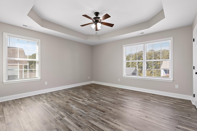 empty room with dark hardwood / wood-style flooring, ceiling fan, plenty of natural light, and a raised ceiling