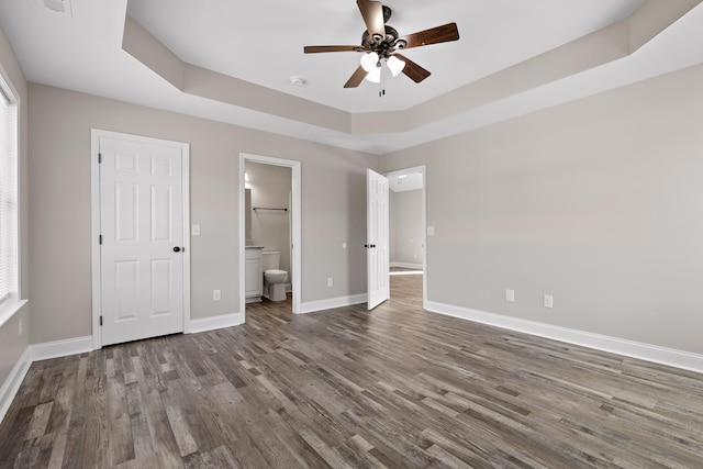 unfurnished bedroom with ensuite bath, hardwood / wood-style flooring, a tray ceiling, and ceiling fan