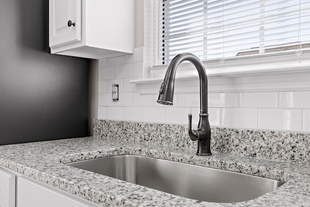 details with decorative backsplash, white cabinets, light stone countertops, and sink