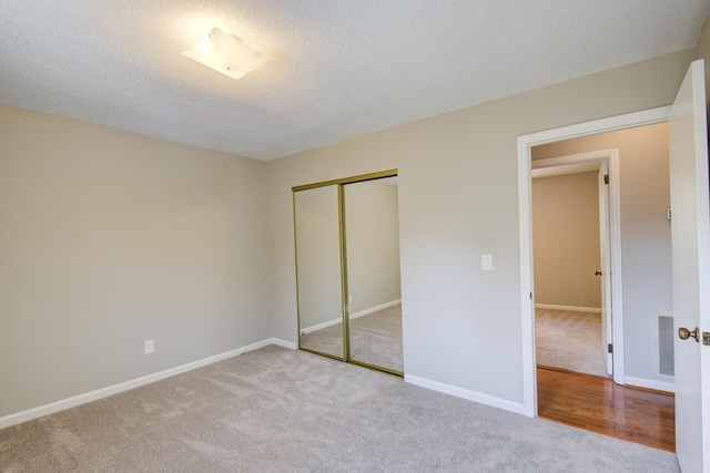 unfurnished bedroom featuring light colored carpet, a textured ceiling, and a closet