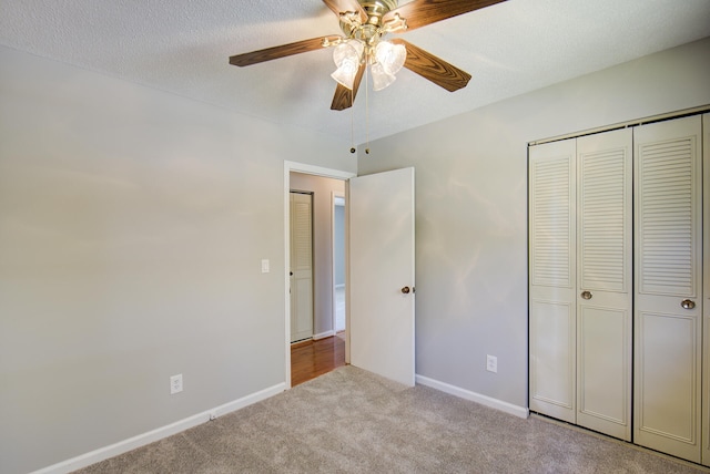 unfurnished bedroom featuring ceiling fan, a closet, light colored carpet, and a textured ceiling