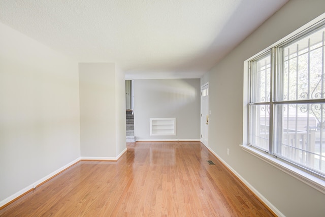 unfurnished room featuring a wealth of natural light, light hardwood / wood-style flooring, and a textured ceiling