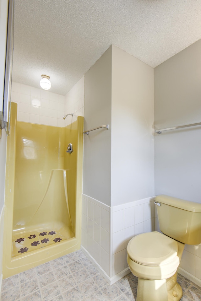 bathroom with a tile shower, a textured ceiling, toilet, and tile walls