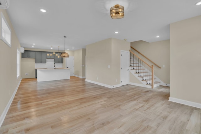 unfurnished living room with a chandelier, light wood-type flooring, and a wall mounted air conditioner