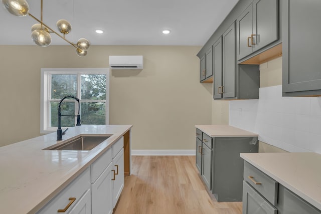 kitchen with sink, tasteful backsplash, light wood-type flooring, an AC wall unit, and decorative light fixtures