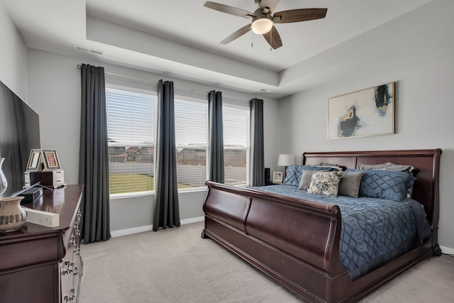 carpeted bedroom with a raised ceiling and ceiling fan