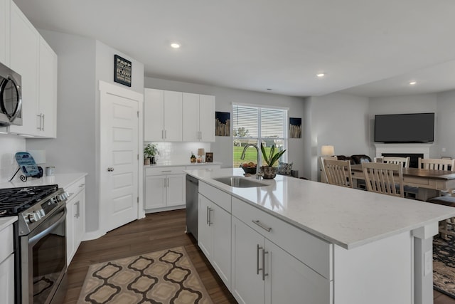 kitchen with white cabinetry, sink, dark hardwood / wood-style flooring, a center island with sink, and appliances with stainless steel finishes