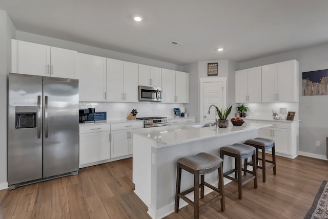 kitchen with stainless steel appliances, a center island with sink, light hardwood / wood-style flooring, white cabinetry, and a breakfast bar area