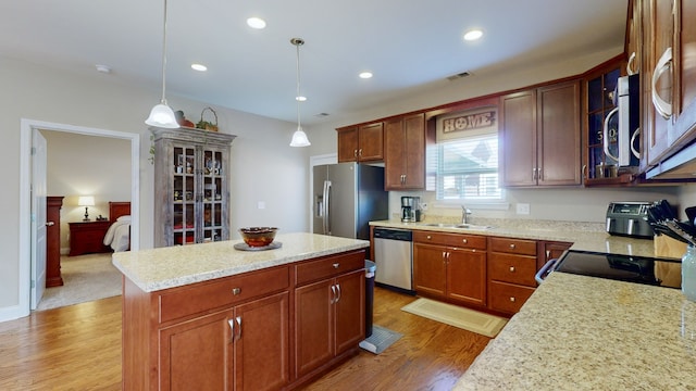 kitchen with hanging light fixtures, light stone countertops, stainless steel appliances, sink, and a center island