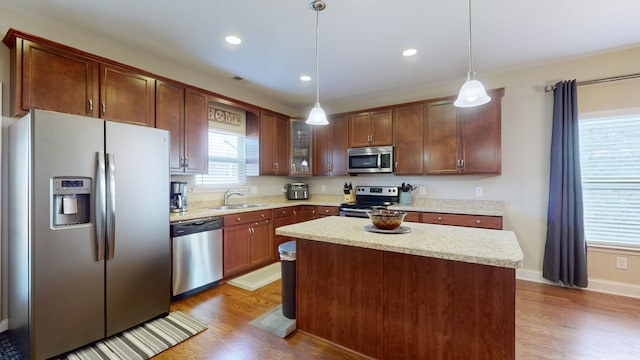 kitchen with hanging light fixtures, a kitchen island, appliances with stainless steel finishes, wood-type flooring, and sink