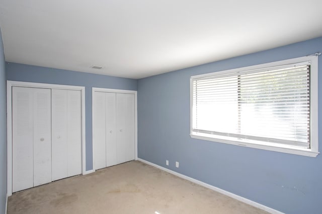 unfurnished bedroom featuring multiple closets and light colored carpet