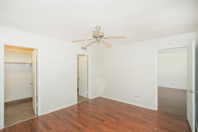 unfurnished bedroom featuring a closet, dark hardwood / wood-style floors, a spacious closet, and ceiling fan