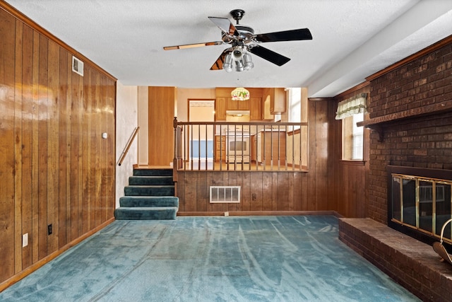 unfurnished living room featuring wood walls, carpet, a textured ceiling, and a fireplace