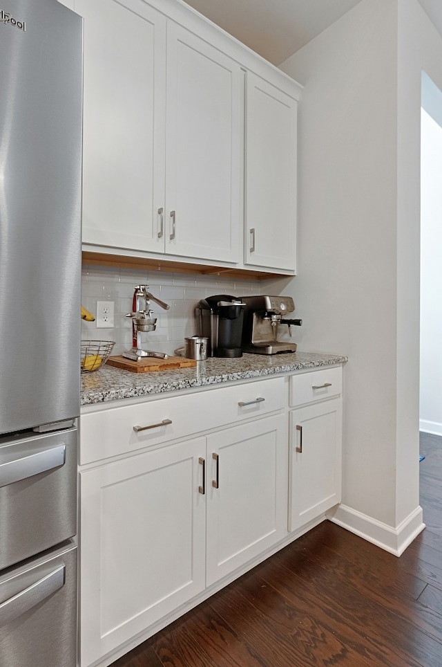 bar featuring backsplash, stainless steel fridge, light stone countertops, white cabinetry, and dark hardwood / wood-style flooring