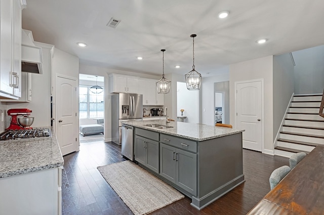 kitchen with appliances with stainless steel finishes, white cabinetry, decorative light fixtures, dark wood-type flooring, and a center island with sink