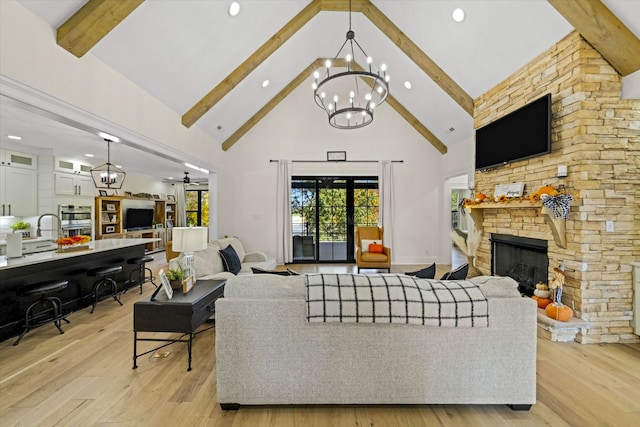 living room featuring ceiling fan with notable chandelier, a fireplace, beamed ceiling, high vaulted ceiling, and light hardwood / wood-style flooring