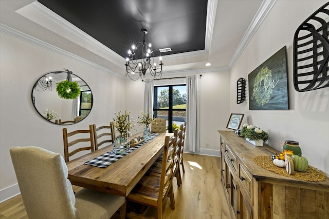 dining area with ornamental molding, a chandelier, light hardwood / wood-style flooring, and a tray ceiling