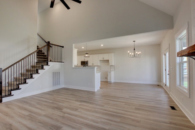 unfurnished living room featuring light wood-type flooring, ceiling fan with notable chandelier, and high vaulted ceiling