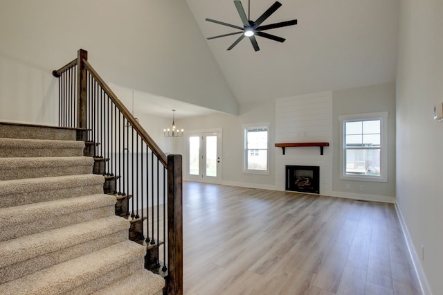 unfurnished living room with a fireplace, ceiling fan with notable chandelier, light hardwood / wood-style flooring, and high vaulted ceiling