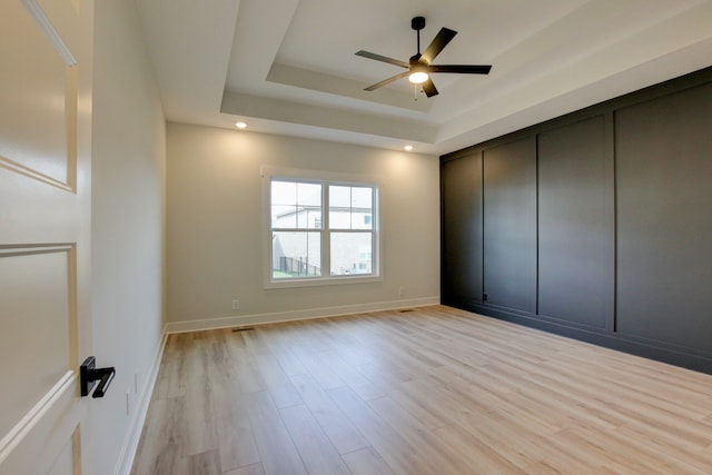 unfurnished bedroom featuring a closet, ceiling fan, a tray ceiling, and light hardwood / wood-style floors