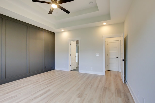 unfurnished bedroom with light hardwood / wood-style floors, ceiling fan, a raised ceiling, and a closet