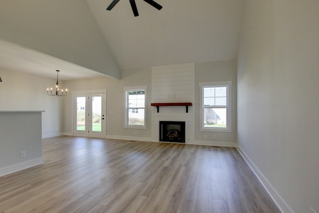 unfurnished living room featuring a fireplace, light hardwood / wood-style floors, ceiling fan with notable chandelier, and high vaulted ceiling