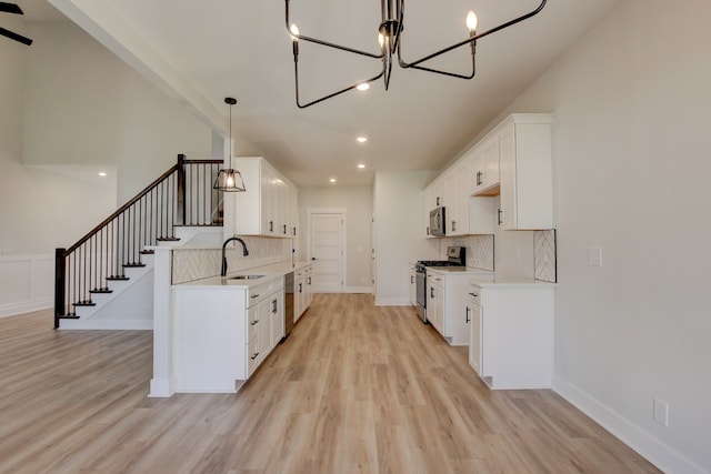 kitchen with light hardwood / wood-style flooring, hanging light fixtures, sink, white cabinetry, and appliances with stainless steel finishes