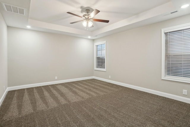 spare room with recessed lighting, a raised ceiling, visible vents, and baseboards