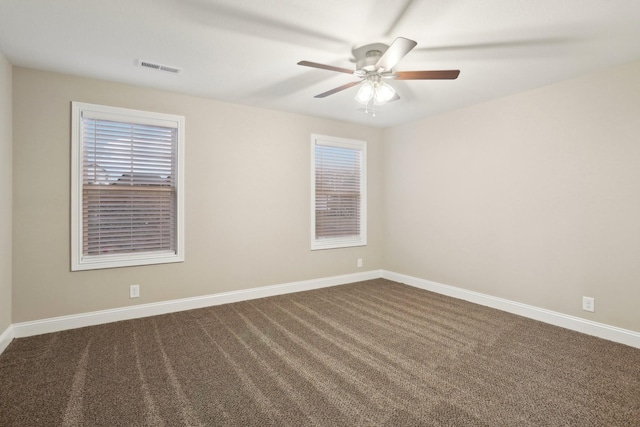 unfurnished room with ceiling fan, dark carpet, visible vents, and baseboards