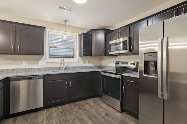 kitchen with stainless steel appliances, a sink, visible vents, light stone countertops, and dark wood-style floors