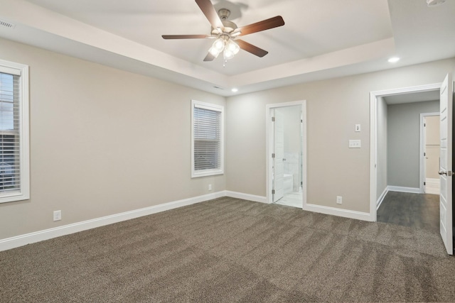 unfurnished bedroom featuring baseboards, a raised ceiling, connected bathroom, dark carpet, and recessed lighting