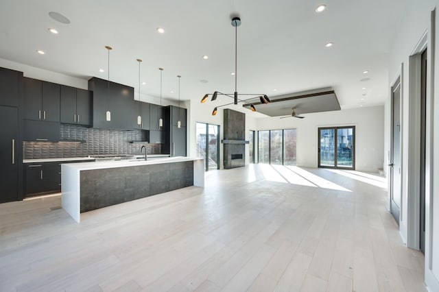 kitchen with a center island with sink, ceiling fan, decorative light fixtures, light wood-type flooring, and tasteful backsplash